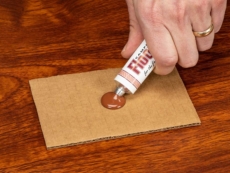 A person squeezes FloorFil laminate floor repair/filler out of a tube.