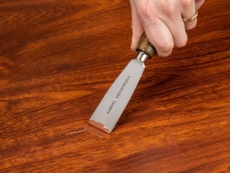 A person applies FloorFil laminate floor repair/filler to the damaged floor with a putty knife.