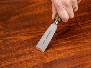A person applies FloorFil laminate floor repair/filler to the damaged floor with a putty knife.